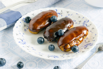 Homemade chocolate eclair with blueberry on colored plate