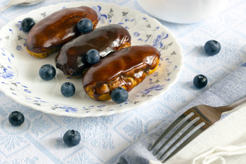 Homemade chocolate eclair with blueberry on colored plate