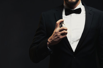 Handsome young man using perfume on black background