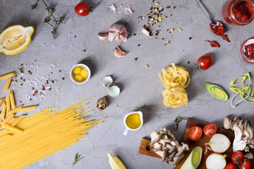 Italian pasta with cooking ingredients. Pastas, spices, tomato sauce and vegetables over grey background. Top view, copy space. Flat lay.
