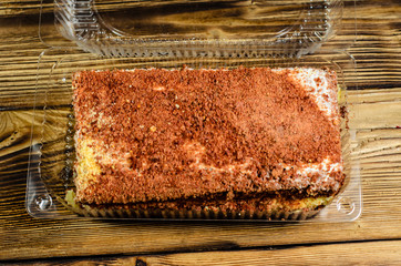 Biscuit cake in plastic container on wooden table. Top view