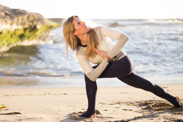 Blonde young woman doing yoga on the beach. Girl in black yoga pans, leggins and white sweater. San Diego, California