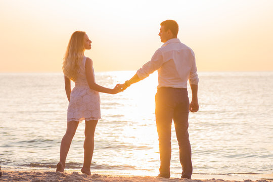 Beautiful young romantic couple holding hands on seaside in rays of rising sun