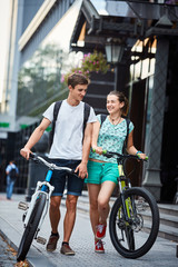 Young people, couple with bicycles on the street. A loving couple on a date on a summer evening. The guy with the girl hugs and kisses. Youth, first feelings, first love, first dates