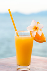 glass of orange juice, decorated with tropical plumeria flower on the beach, concept luxury vacation
