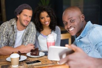 Fototapeta premium Friends taking selfie at wooden table in coffee shop