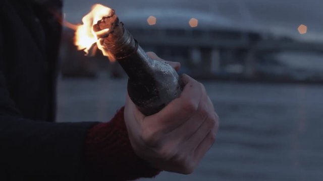 Hand of young man clutching burning Molotov cocktail bottlestanding on coast