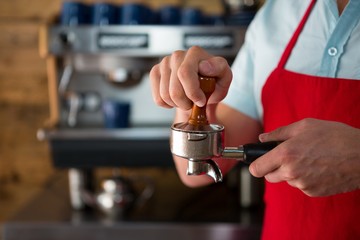 Barista using tamper to press ground coffee 