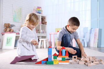 Cute little sister and brother playing with toy blocks at home