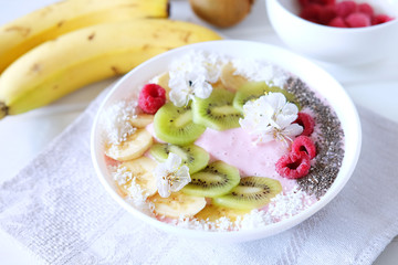 Raspberry and banana smoothie bowl with kiwi slices, shredded coconut and chia seeds.