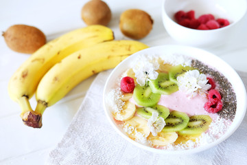 Raspberry and banana smoothie bowl with kiwi slices, shredded coconut and chia seeds.