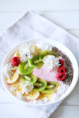 Raspberry and banana smoothie bowl with kiwi slices, shredded coconut and chia seeds.