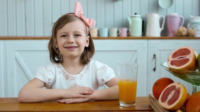 Adorable little girl drinking orange juice on breakfast on morning, small child drink, fruits on table