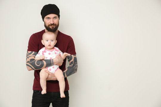 Handsome Tattooed Young Man Holding Cute Little Baby On Light Background