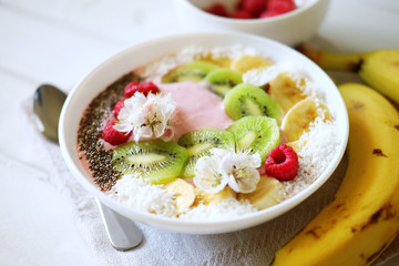Raspberry and banana smoothie bowl with kiwi slices, shredded coconut and chia seeds.