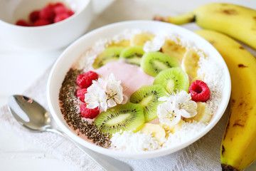 Raspberry and banana smoothie bowl with kiwi slices, shredded coconut and chia seeds.