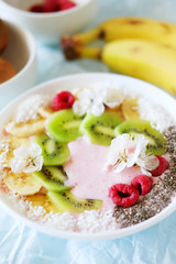 Raspberry and banana smoothie bowl with kiwi slices, shredded coconut and chia seeds.