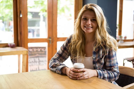 Smiling young woman holding disposable coffee cup in cafe