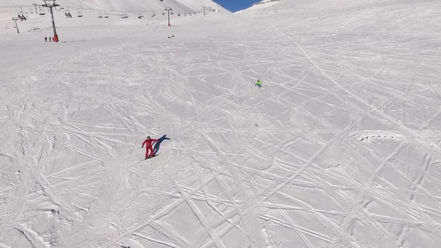 Two males riding snowboard and ski from slope with poma lift on background in slowmotion