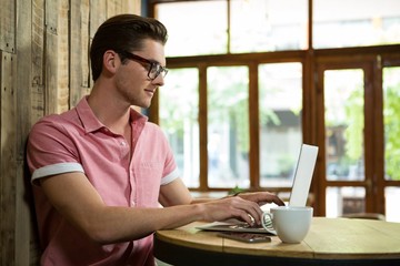 Handsome young man using laptop at table in coffee shop