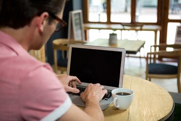 Obraz na płótnie Canvas Man using laptop at table in coffee shop