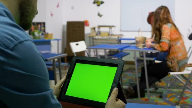 Teenager sitting at desk in a class room and swiping the display of a tablet pc