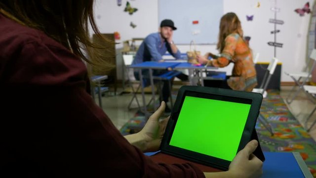 Teenagers in classroom socializing with green screen tablet pc