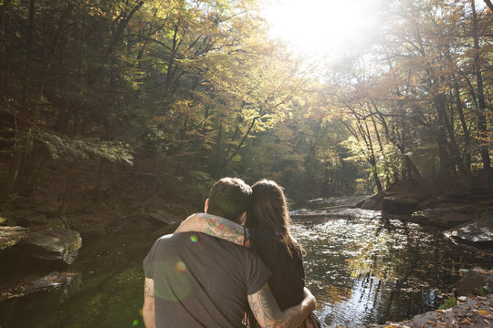 Rear view of young couple sitting near stream at forest