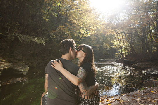 Young couple kissing while sitting near stream in forest