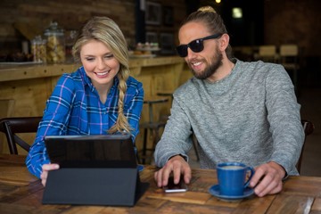 Smiling couple using tablet computer at table in cafeteria