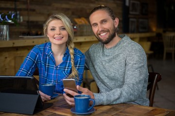 Portrait of smiling couple with coffee and technologies in cafe