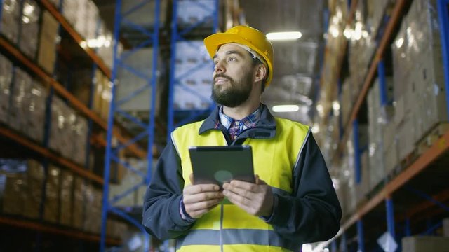Auditor Wearing Hard Hat Looking around Warehouse and Using Tablet Computer. Rows of Storage Racks are Seen. Shot on RED EPIC-W 8K Helium Cinema Camera.