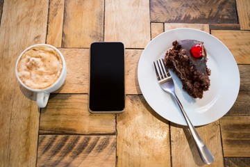 Smart phone with pastry and coffee cup on table