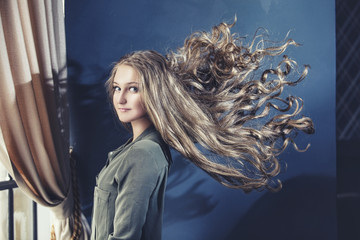 Portrait of young blonde woman with developing with a wavy long hair on gray background