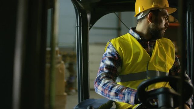 Close-up Shot of a Forklift Driver Professionally Operating Vehicle in a Big Warehouse full of Racks with Pallets