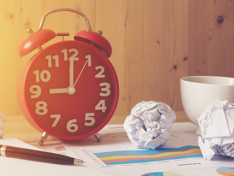 Alarm Clock With Cramped Paper And Stock Graph Chart On Wooden Background.