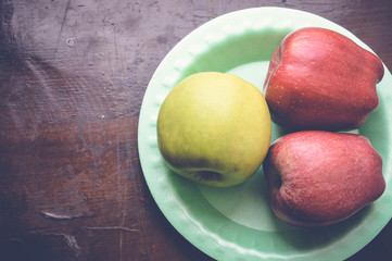 top view of red and green apples on green plate on wooden table