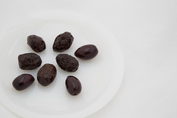  few dark black olives on a white plate and three green spikes on a white mesh background with an empty place for the inscription