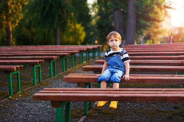 The boy sits on a bench and thinks about something