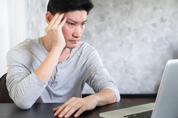 Casual young man using laptop on the desk and thinking while working in home office.