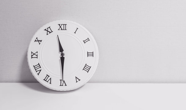 Closeup white clock for decorate show half past eleven o'clock or 11:30 a.m. on white wood desk and wallpaper textured background in black and white tone with copy space