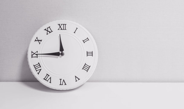 Closeup white clock for decorate show a quarter to twelve o'clock or 11:45 a.m. on white wood desk and wallpaper textured background in black and white tone with copy space