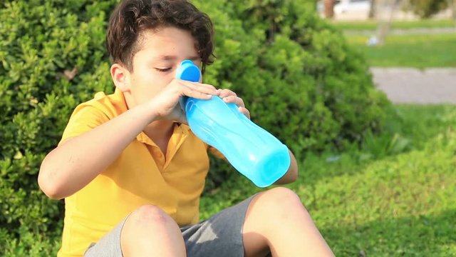 Portrait of a cute child drinking water from a bottle outdoor and smiling