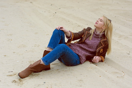 Young sexy blonde girl in nature and reeds near a river and trees in American country style in a leather jacket, sweater blue jeans and brown boots with a beautiful face and pretty eyes