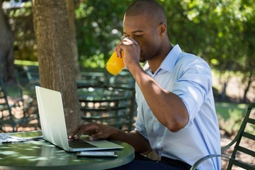 Man drinking juice while using laptop at restaurant