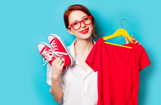 photo of beautiful young woman holding shirt on hanger and gumshoes on the wonderful blue studio background