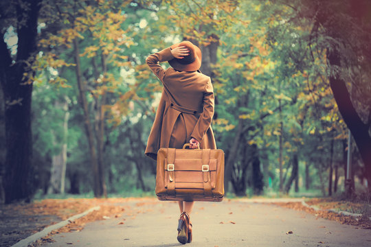 photo of beautiful young woman with suitcase on the wonderful autumn park background