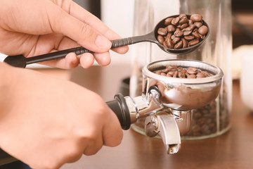 Barista pouring roasted coffee bean from spoon in to a portafilter prepare for making coffee from espresso machine