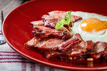 Slices of smoked bacon and fried egg on a red plate