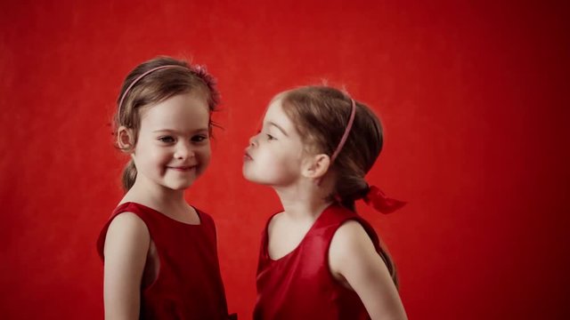 Two little girls kissing on a red background
